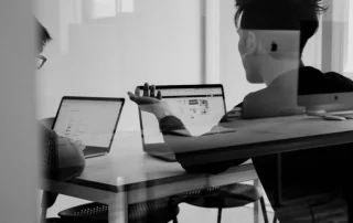 two people sat at a desk at laptops making a crucial decision